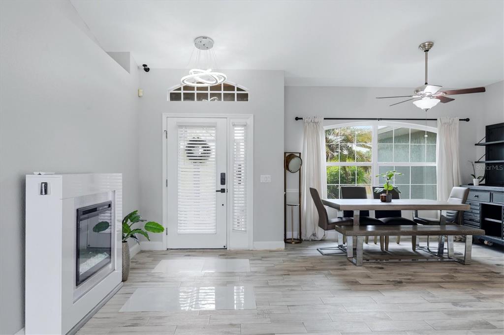 A bright dining area features a white fireplace, a modern chandelier, and wood-look tile flooring — 8188 WELSFORD ROAD, PORT CHARLOTTE, FL