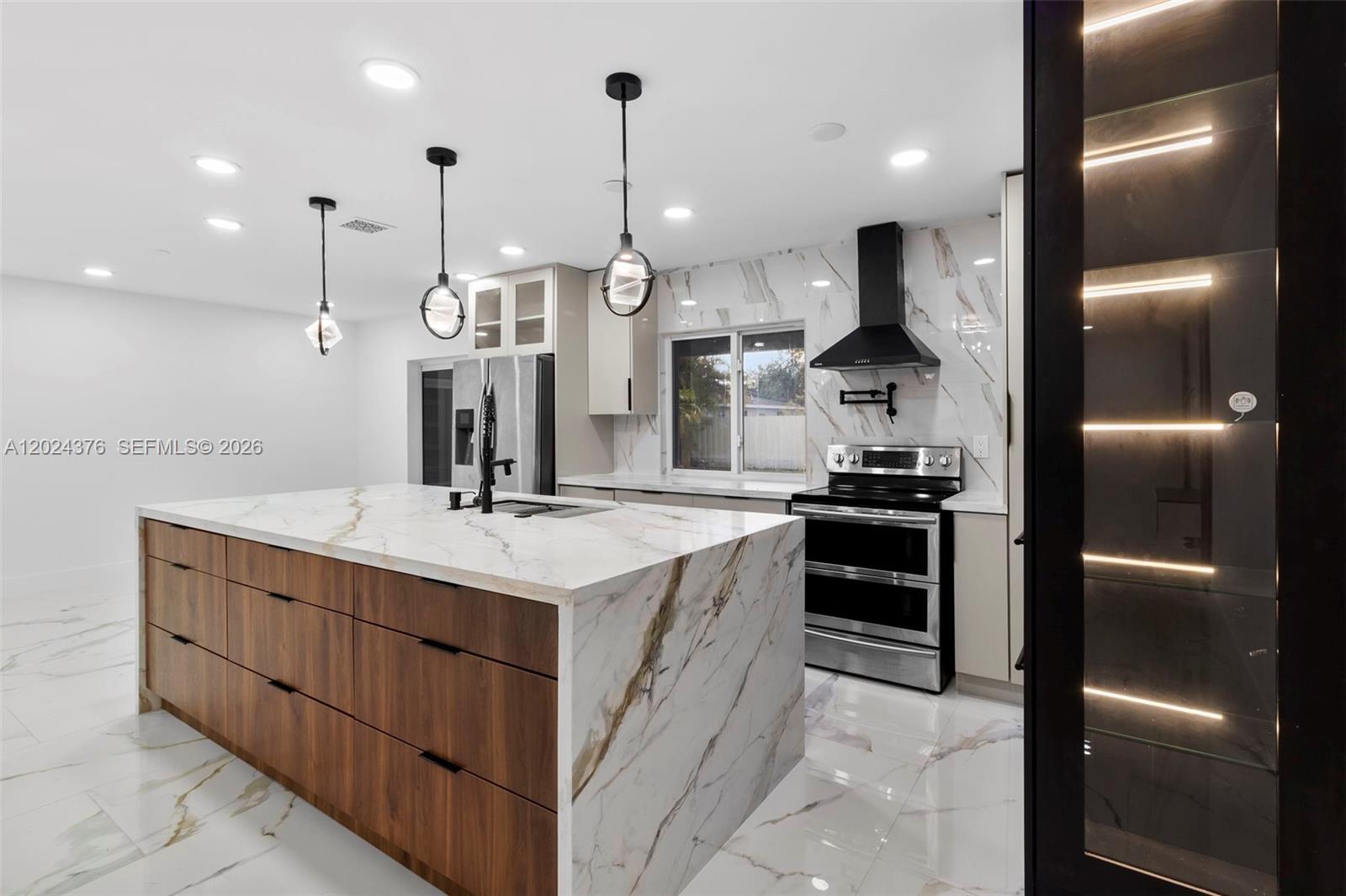 A modern kitchen features a large marble-topped island, wood cabinetry, and stainless steel appliances — 7220 NW 10th Pl, Plantation FL 33313, PLANTATION, FL