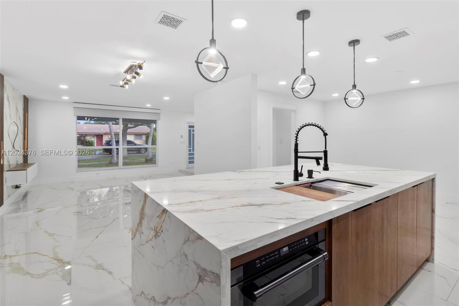 A modern kitchen features a marble waterfall island with a built-in oven and pendant lights — 7220 NW 10th Pl, Plantation FL 33313, PLANTATION, FL