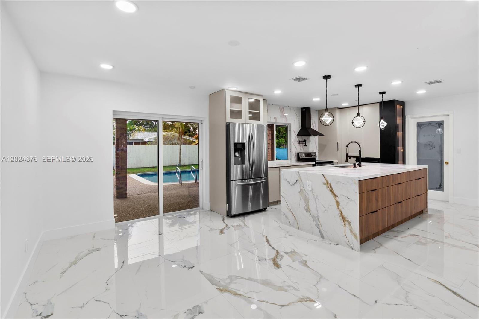 A modern kitchen features a marble waterfall island, wood cabinetry, and white tile flooring — 7220 NW 10th Pl, Plantation FL 33313, PLANTATION, FL