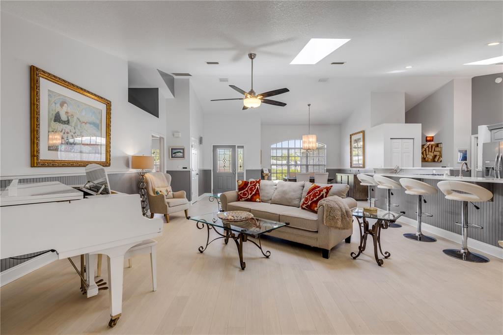 A spacious living room features a white grand piano, beige sofa, and kitchen breakfast bar — 815 E 7TH AVENUE, NEW SMYRNA BEACH, FL