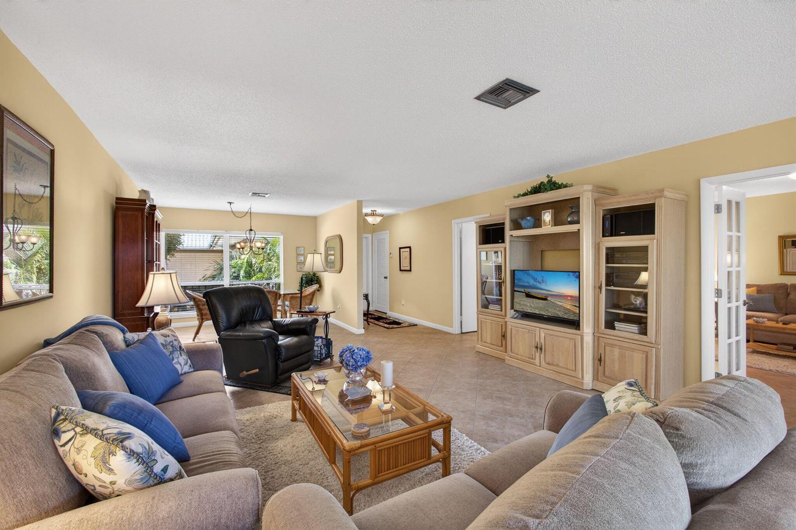 A living room features beige walls, tile flooring, a beige sofa, and a wooden entertainment center — 17 SE Turtle Creek Drive Unit D, Jupiter FL 33469, JUPITER, FL