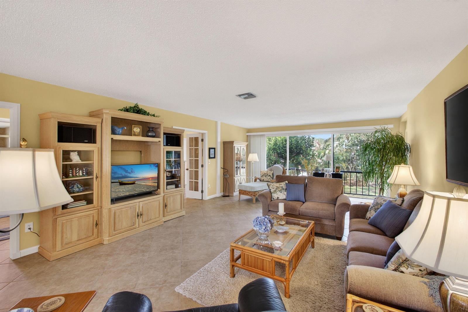 A living room features light tile floors, a large wooden entertainment center, and brown sofas — 17 SE Turtle Creek Drive Unit D, Jupiter FL 33469, JUPITER, FL