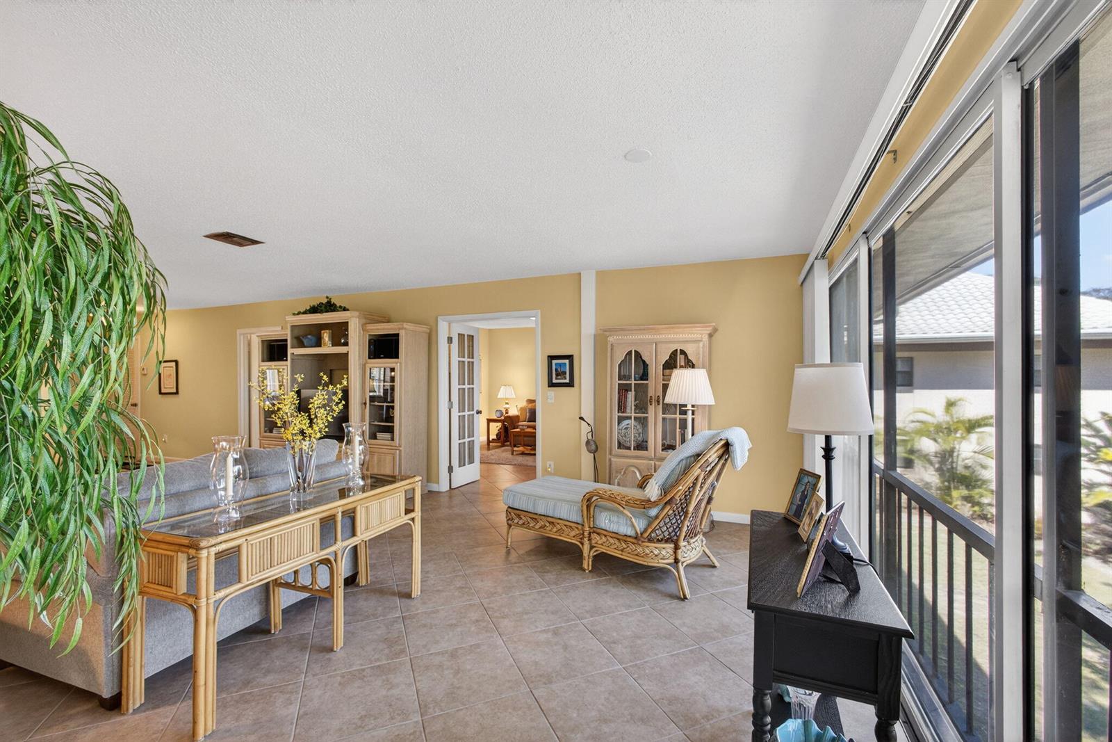 A living room with tile floors, a rattan chaise lounge, and a large indoor plant — 17 SE Turtle Creek Drive Unit D, Jupiter FL 33469, JUPITER, FL
