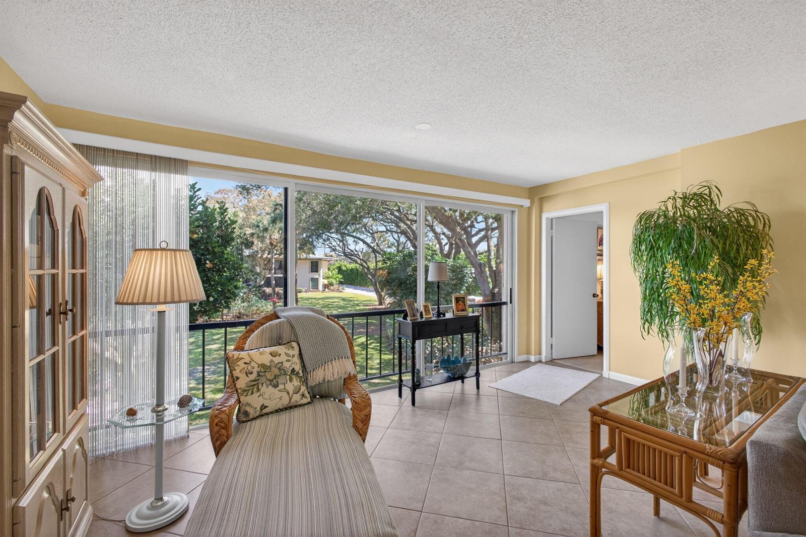 A sunroom with tile floors, a wicker chaise lounge, and sliding glass doors overlooking trees — 17 SE Turtle Creek Drive Unit D, Jupiter FL 33469, JUPITER, FL