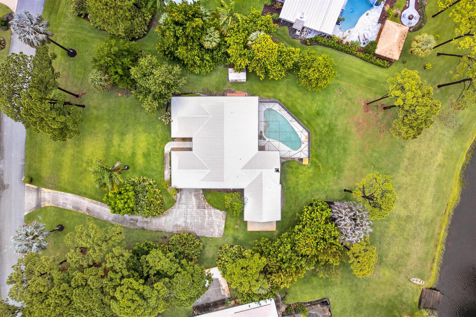 An aerial view shows a house with a metal roof, pool enclosure, and large yard — 441 NE Town Terrace, Jensen Beach FL 34957, JENSEN BEACH, FL