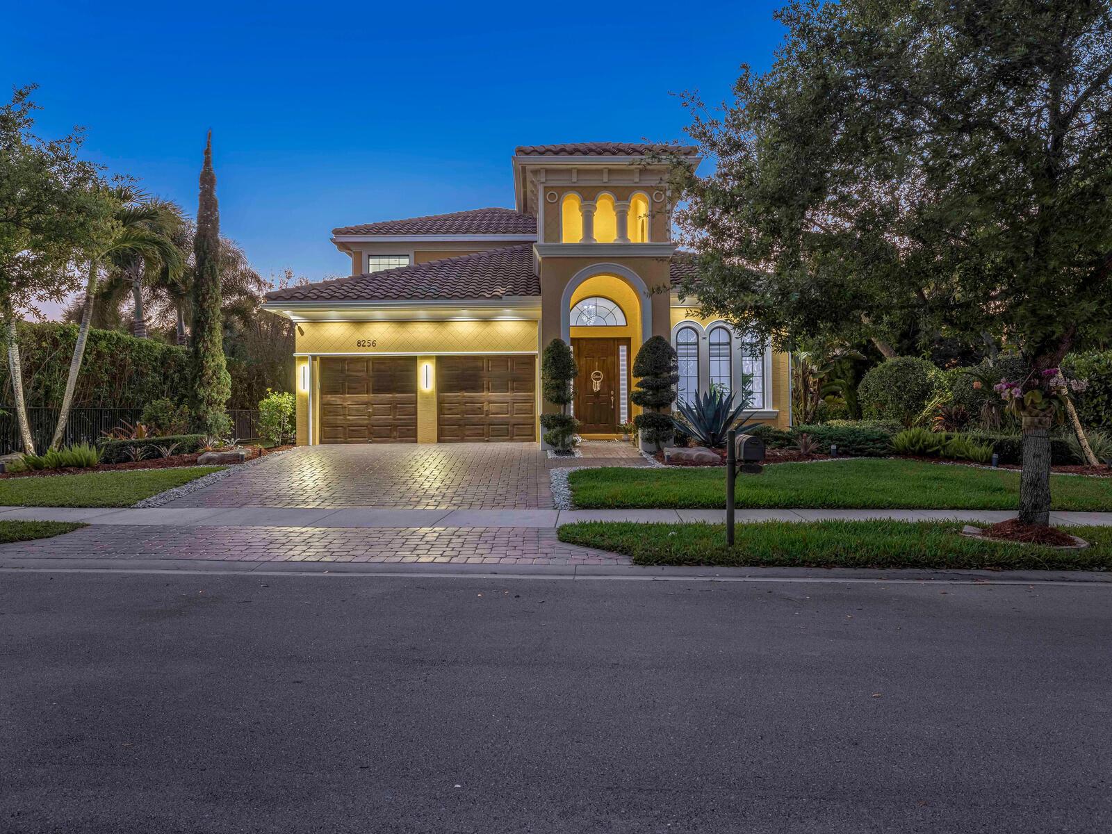 A two-story stucco house with a tile roof, arched entryway, and a paved driveway at dusk — 8256 Bradford Way, Parkland FL 33076, PARKLAND, FL