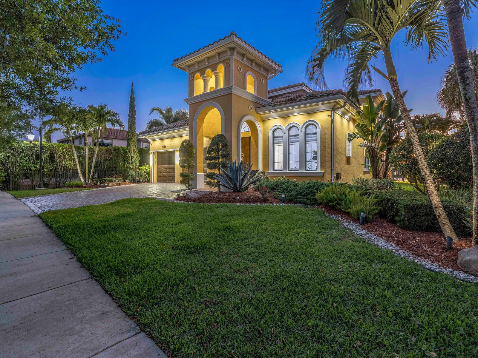 A yellow Mediterranean-style house with a tower, arched entryway, and palm trees at dusk — 8256 Bradford Way, Parkland FL 33076, PARKLAND, FL