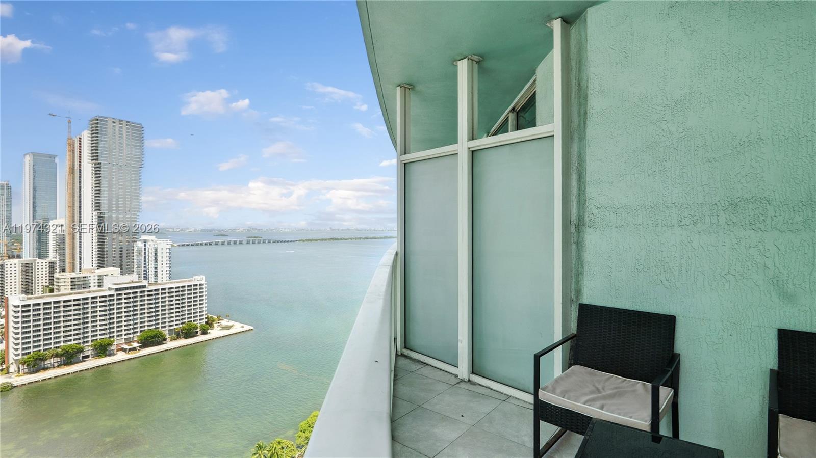 A high-rise balcony features a tiled floor, two chairs, and a view of the bay — 1900 N Bayshore Dr # 2810, Miami FL 33132, MIAMI, FL