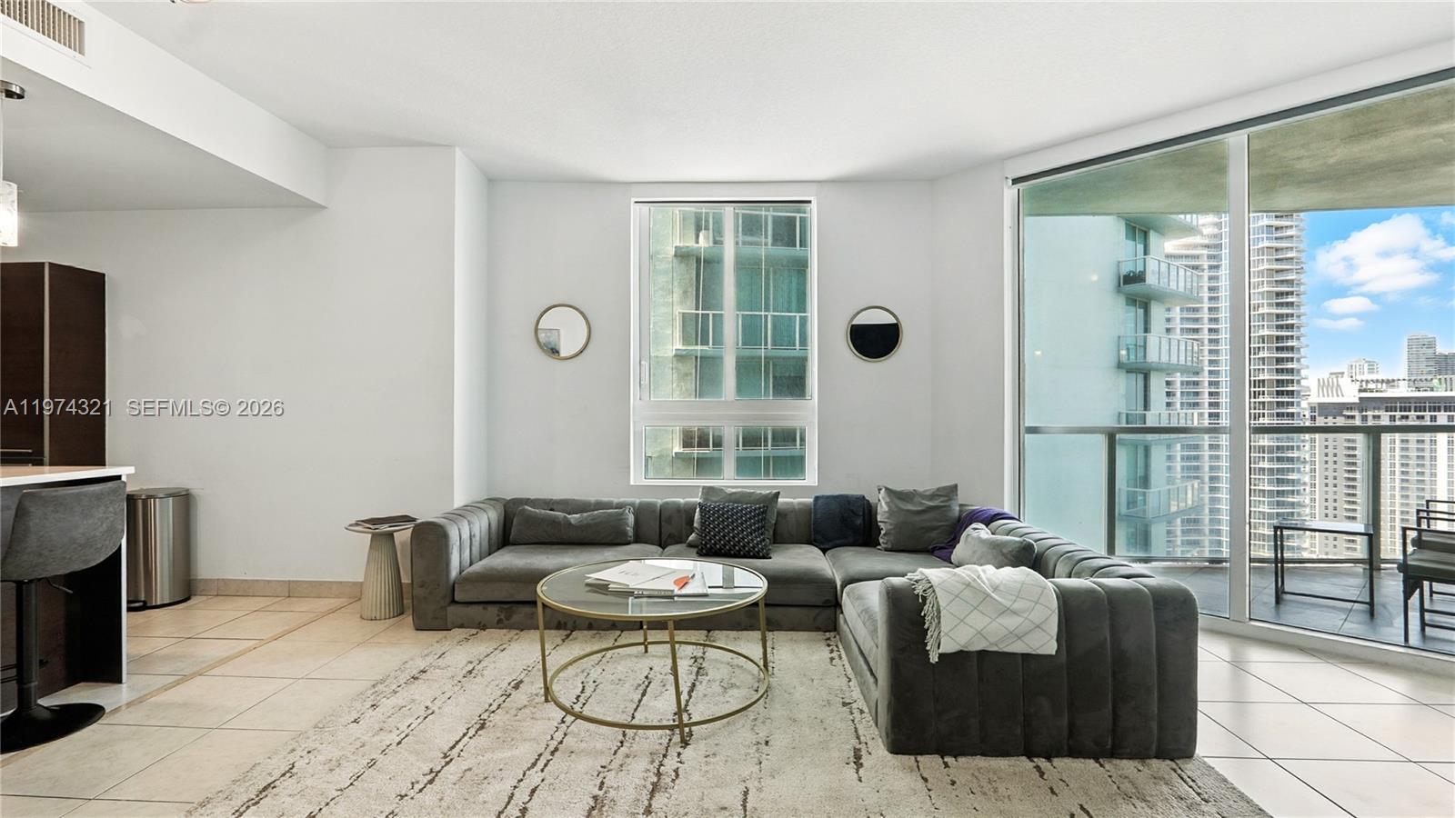A modern living room features a grey sectional sofa, glass coffee table, and floor-to-ceiling windows — 1900 N Bayshore Dr # 2810, Miami FL 33132, MIAMI, FL