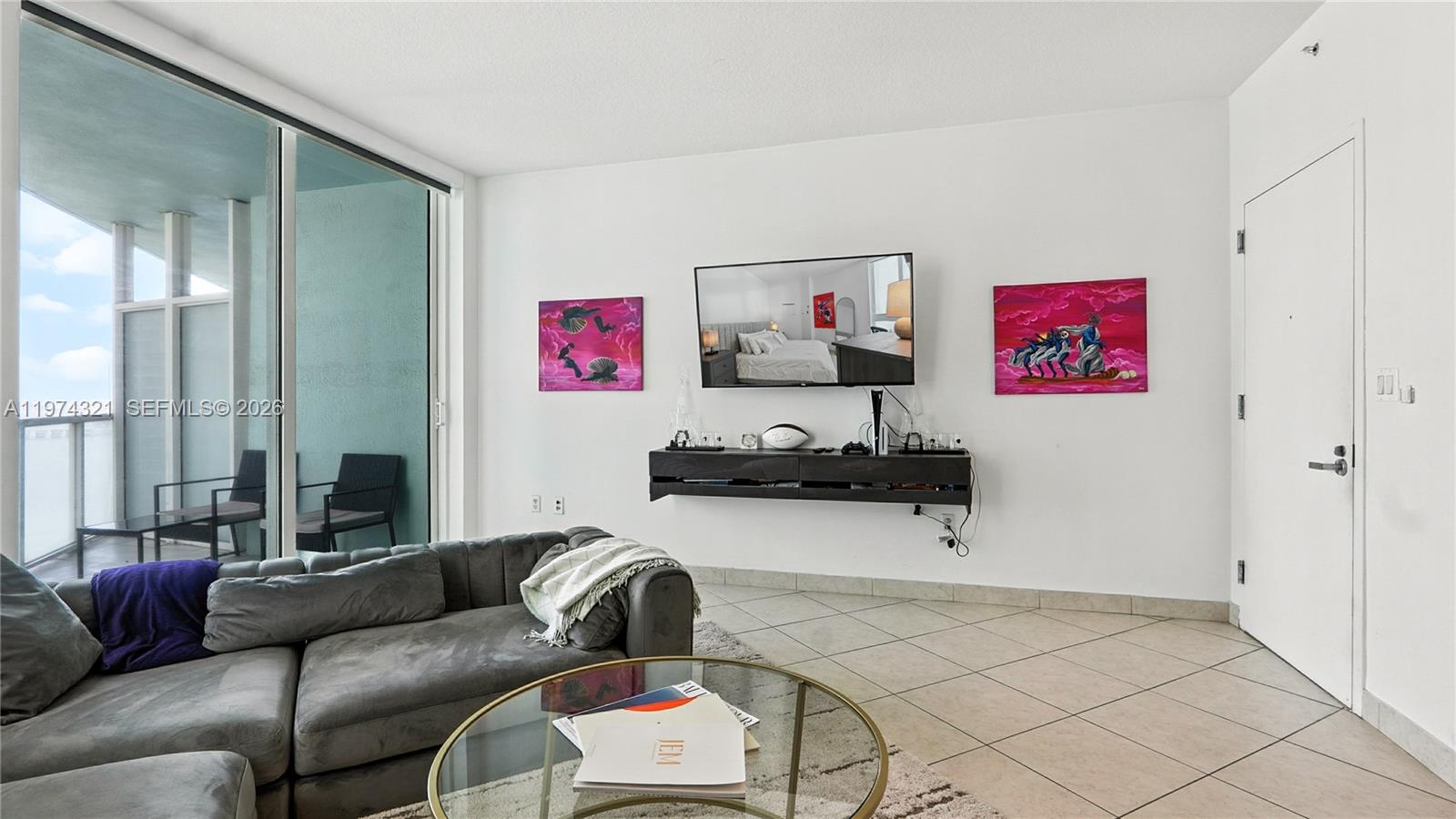 A living room features a grey sectional sofa, a wall-mounted television, and a balcony view — 1900 N Bayshore Dr # 2810, Miami FL 33132, MIAMI, FL