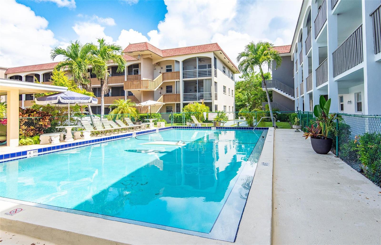 A rectangular swimming pool sits in front of multi-story apartment buildings with palm trees — 651 Pine Drive # 306, Pompano Beach FL 33060, POMPANO BEACH, FL