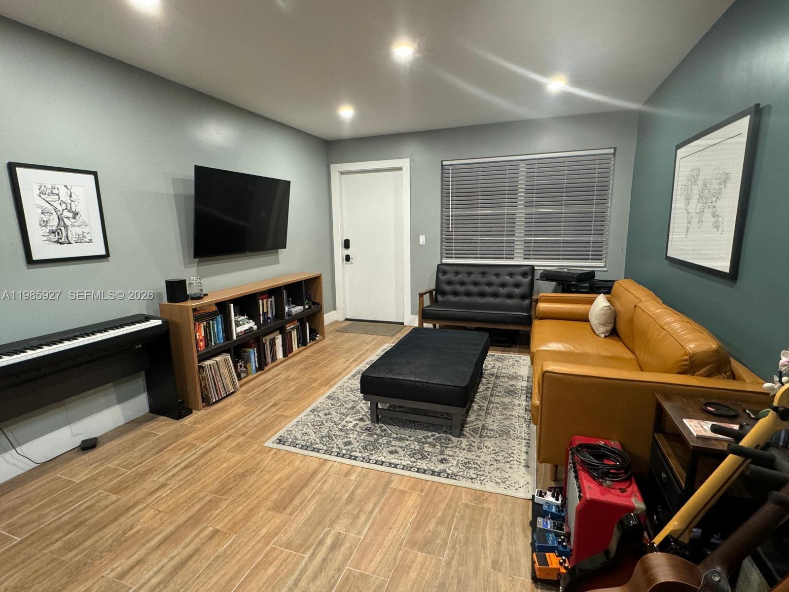 A living room features a tan leather sofa, black furniture, a piano, and wood-look flooring — 2840 Taylor St # 28, Hollywood FL 33020, HOLLYWOOD, FL