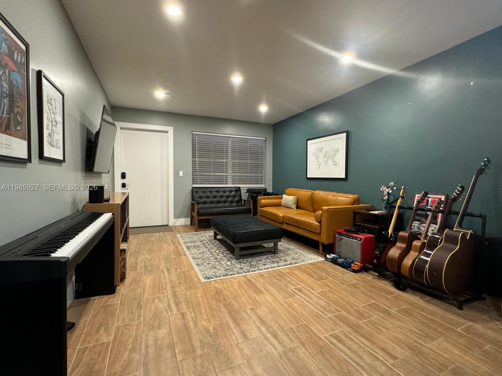 A living room features a tan leather sofa, a black ottoman, and several musical instruments — 2840 Taylor St # 28, Hollywood FL 33020, HOLLYWOOD, FL