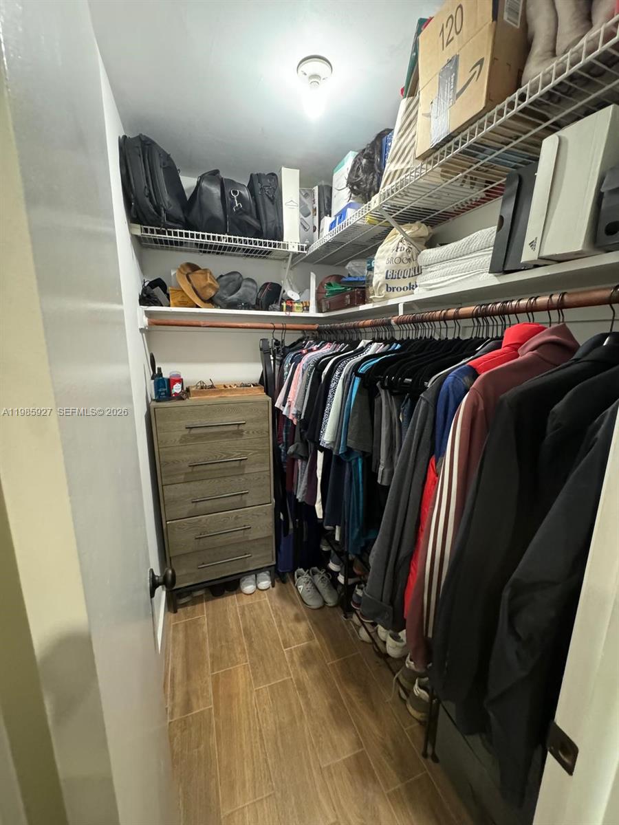 A walk-in closet features wooden flooring, a dresser, hanging clothes, and wire shelving — 2840 Taylor St # 28, Hollywood FL 33020, HOLLYWOOD, FL