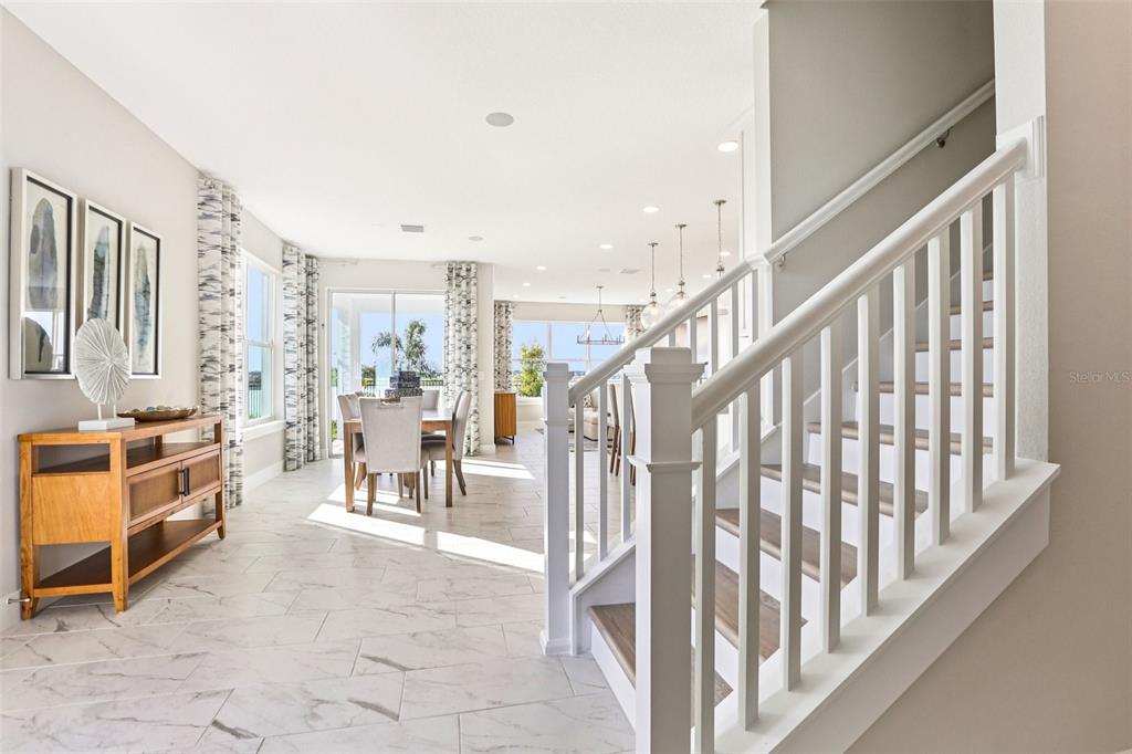 A staircase with white railings overlooks a dining area with tile floors and large windows — 31515 SPANISH MISSION ROAD, SAN ANTONIO, FL