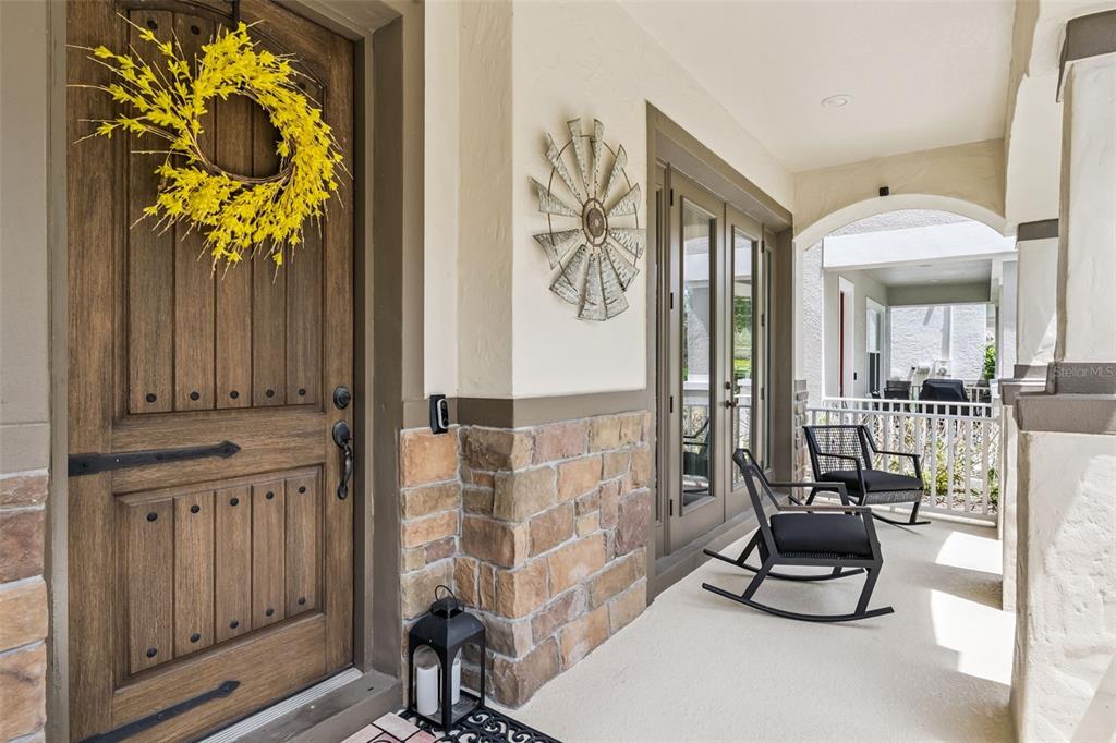 A covered porch features a wooden front door, stone siding, and two black rocking chairs — 9354 MEADOW HUNT WAY, WINTER GARDEN, FL