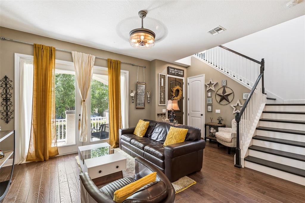 A living room features a leather sofa, a staircase, and floor-to-ceiling windows with yellow curtains — 9354 MEADOW HUNT WAY, WINTER GARDEN, FL