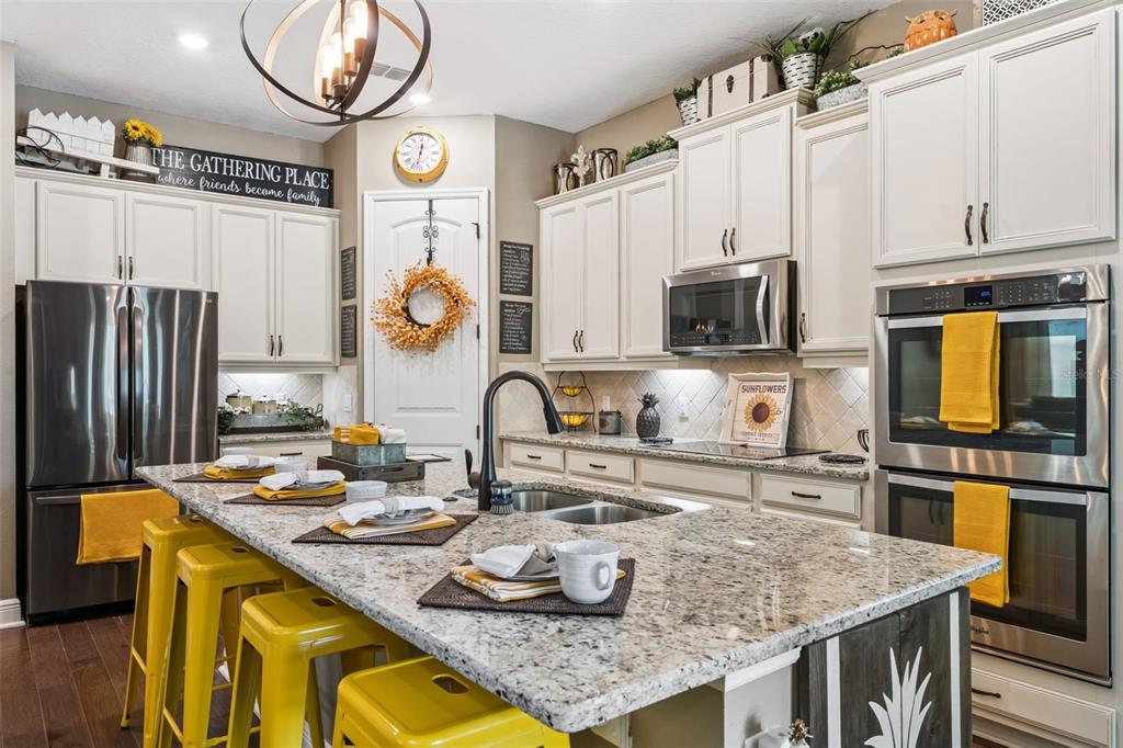 A kitchen features white cabinetry, granite countertops, a central island with yellow stools, and stainless appliances — 9354 MEADOW HUNT WAY, WINTER GARDEN, FL