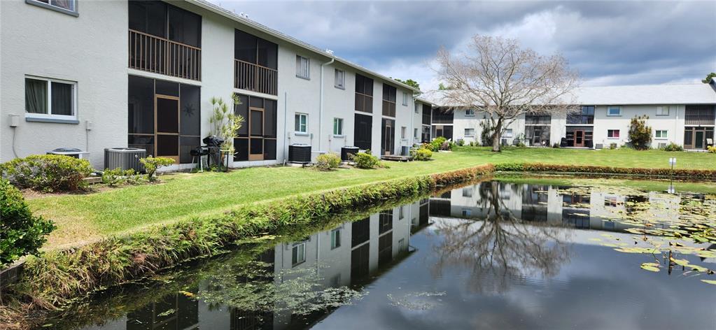 A multi-story apartment building with screened balconies overlooks a small pond with lily pads — 11201 122ND AVENUE UNIT L-232, LARGO, FL