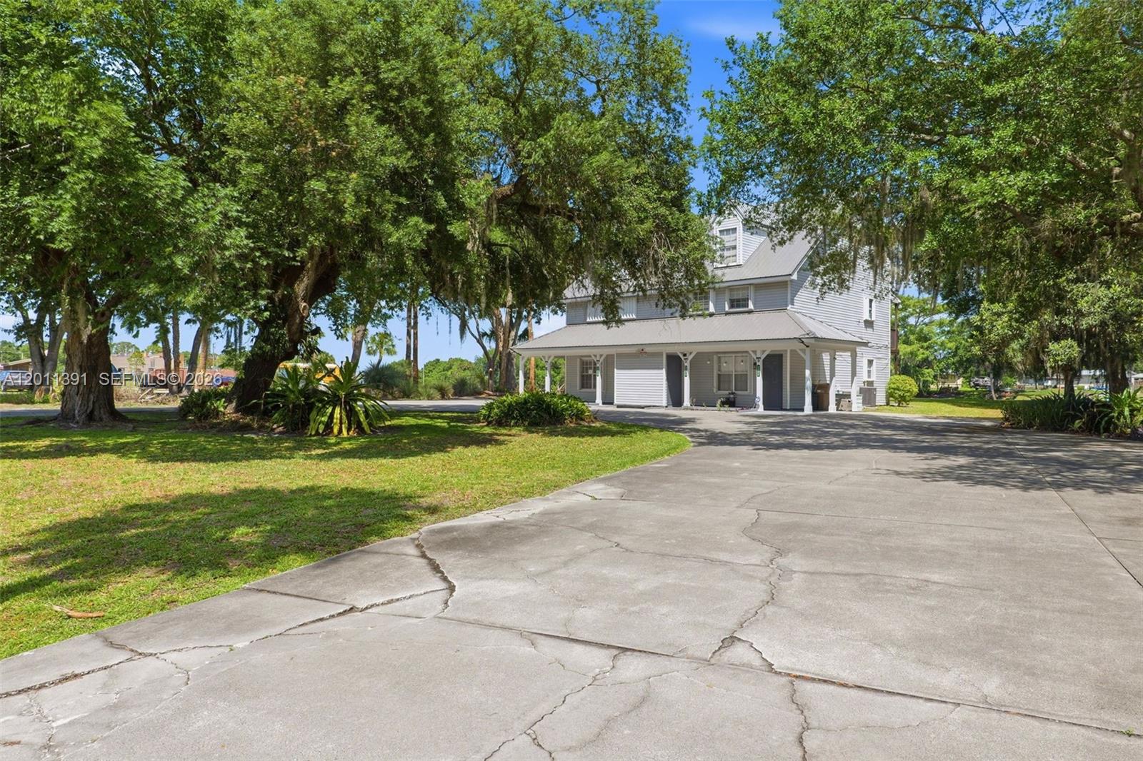 A two-story light gray house with a metal roof sits behind a large cracked driveway — 207 SE 6TH Avenue, Okeechobee FL 34974, OKEECHOBEE, FL