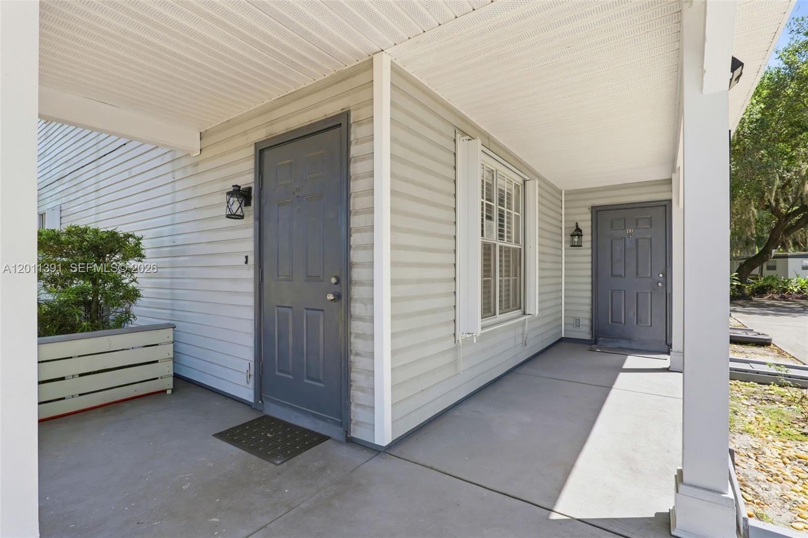 A covered porch features two gray entry doors, light-colored siding, and a concrete floor — 207 SE 6TH Avenue, Okeechobee FL 34974, OKEECHOBEE, FL