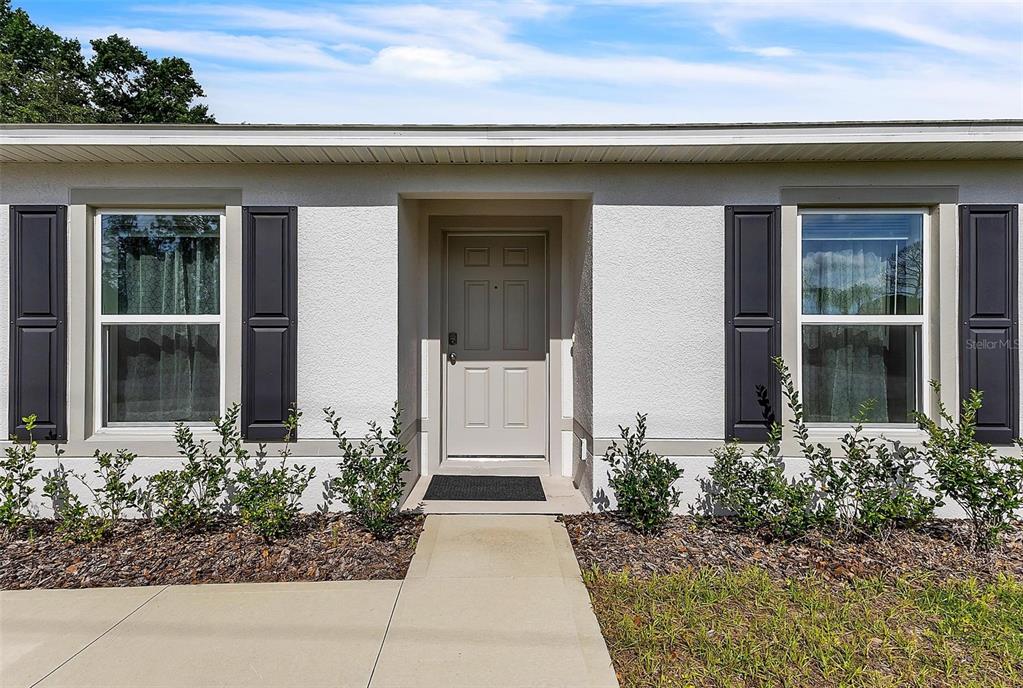 A light-colored house exterior features a front door, two windows with shutters, and landscaping — 22 ROUND TREE DRIVE, PALM COAST, FL