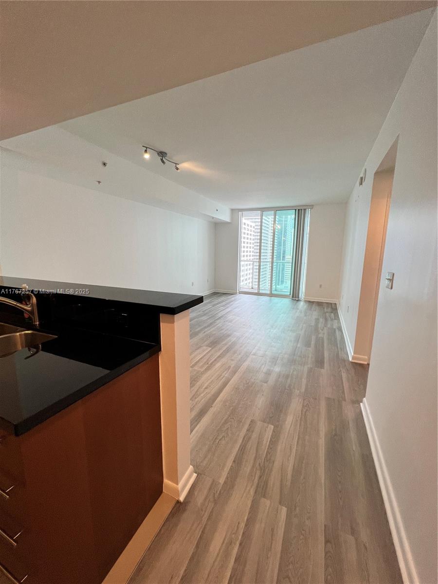 A kitchen with dark countertops overlooks an empty living area with wood-look flooring — 244 Biscayne Blvd # 2609, Miami FL 33132, MIAMI, FL
