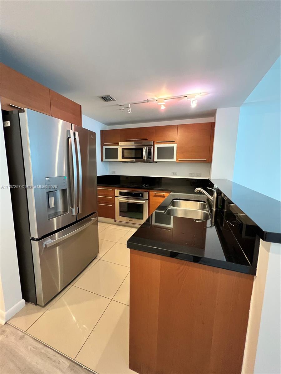 A kitchen features stainless steel appliances, wood cabinetry, and black countertops over tile flooring — 244 Biscayne Blvd # 2609, Miami FL 33132, MIAMI, FL