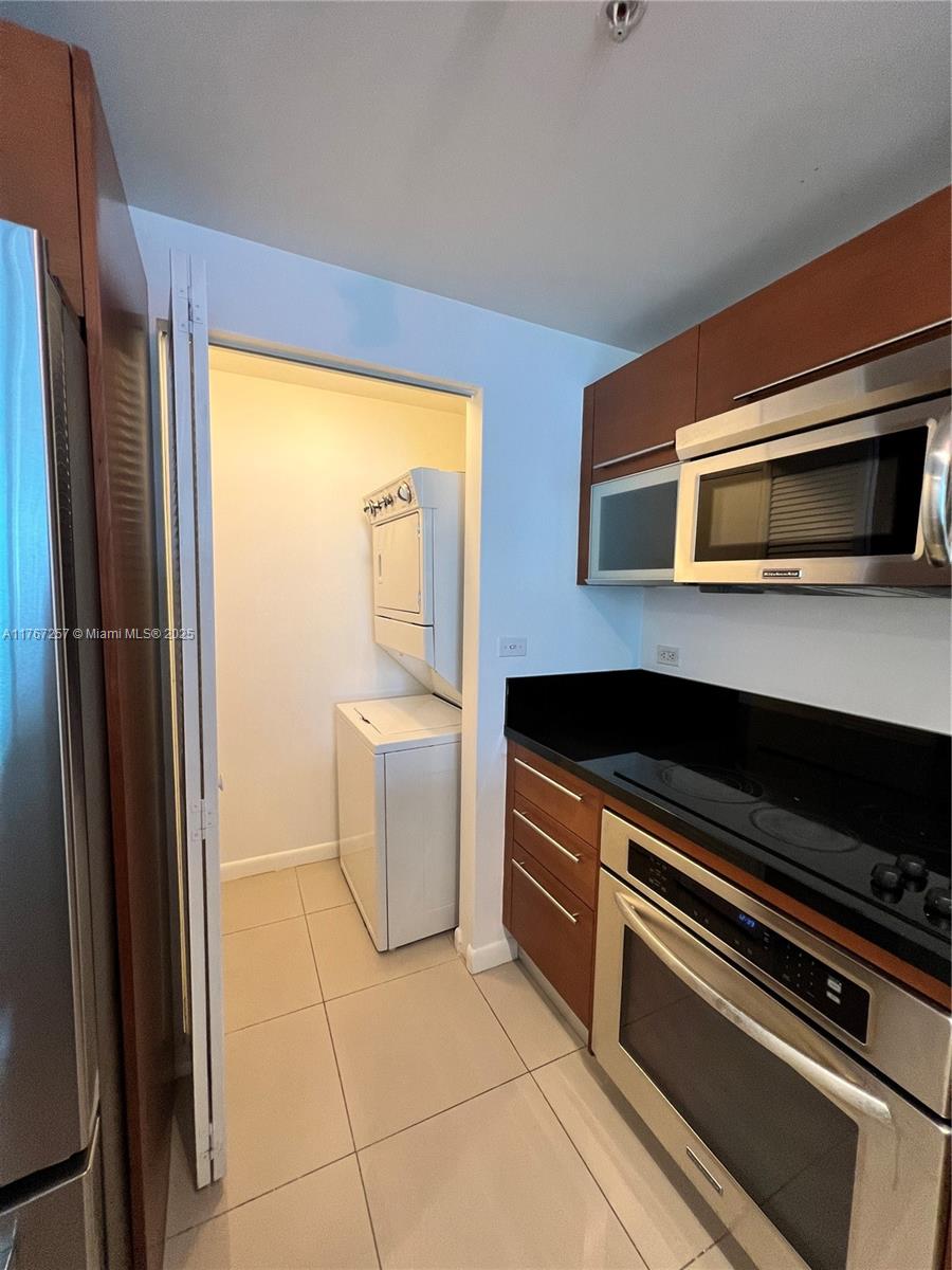 A kitchen with dark wood cabinets and stainless steel appliances leads to a laundry closet — 244 Biscayne Blvd # 2609, Miami FL 33132, MIAMI, FL