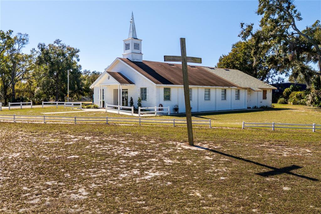 A white church building with a steeple stands behind a large wooden cross — 6104 POLK AVENUE NW, LAKELAND, FL