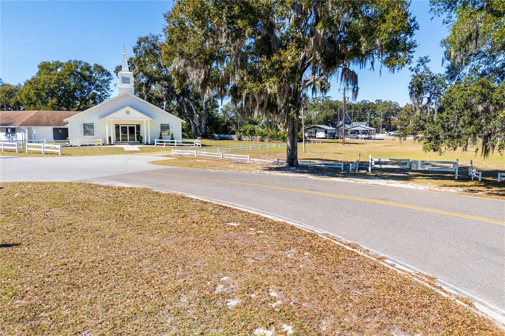 A white church building sits beside a paved road under a large, moss-draped tree — 6104 POLK AVENUE NW, LAKELAND, FL