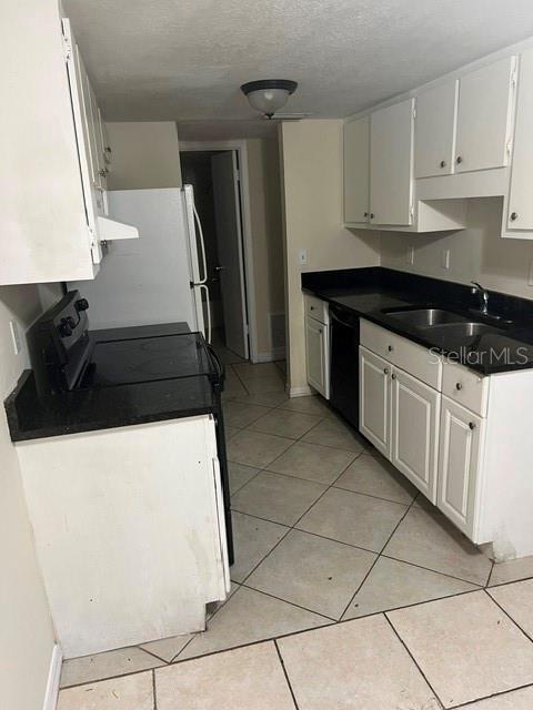 A kitchen features white cabinets, black countertops, tile flooring, and a white refrigerator — 5206 CURRY FORD ROAD UNIT 113, ORLANDO, FL