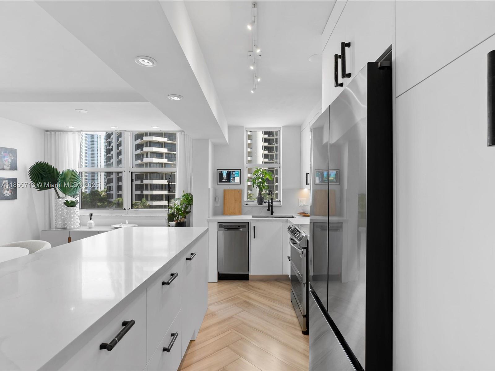 A modern kitchen features white cabinetry, a large island, stainless steel appliances, and herringbone flooring — 770 Claughton Island Dr # 701, Miami FL 33131, MIAMI, FL