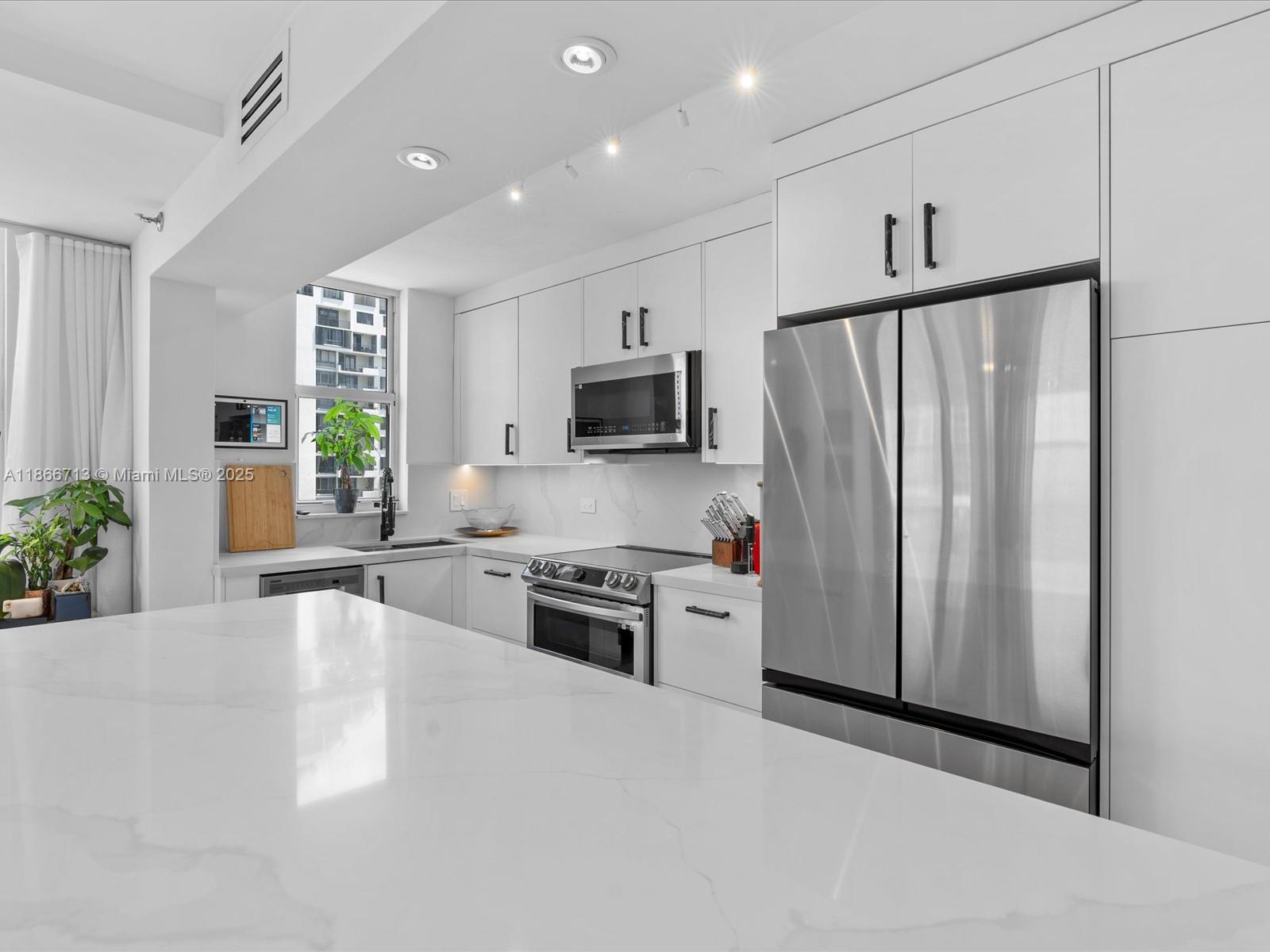 A modern kitchen features white cabinetry, stainless steel appliances, and a large marble-topped island — 770 Claughton Island Dr # 701, Miami FL 33131, MIAMI, FL