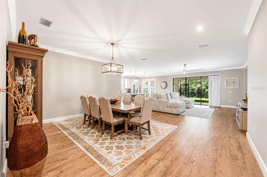 An open-concept dining and living area features wood flooring, a rectangular table, and sliding doors — 3870 BOWFIN TRAIL, KISSIMMEE, FL