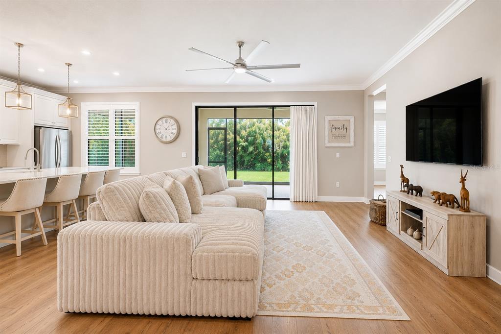 A living room with a large sectional sofa, wood flooring, and a wall-mounted television — 3870 BOWFIN TRAIL, KISSIMMEE, FL