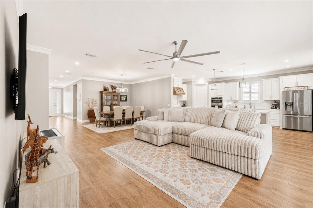 An open-concept living room and dining area with light wood flooring and a sectional sofa — 3870 BOWFIN TRAIL, KISSIMMEE, FL