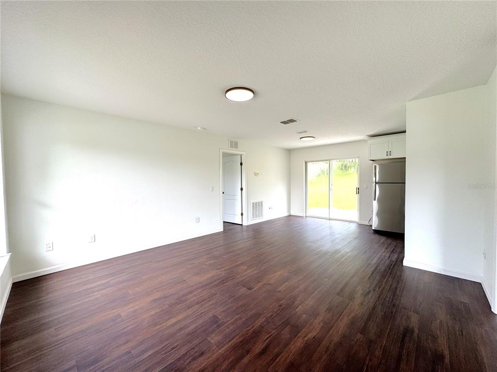 An open-concept living area features dark wood-look flooring, white walls, and a stainless steel refrigerator — 102 EDISON STREET, INVERNESS, FL