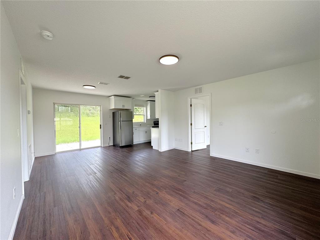 An open-concept living area features wood-look flooring, white walls, and a kitchen with stainless appliances — 102 EDISON STREET, INVERNESS, FL