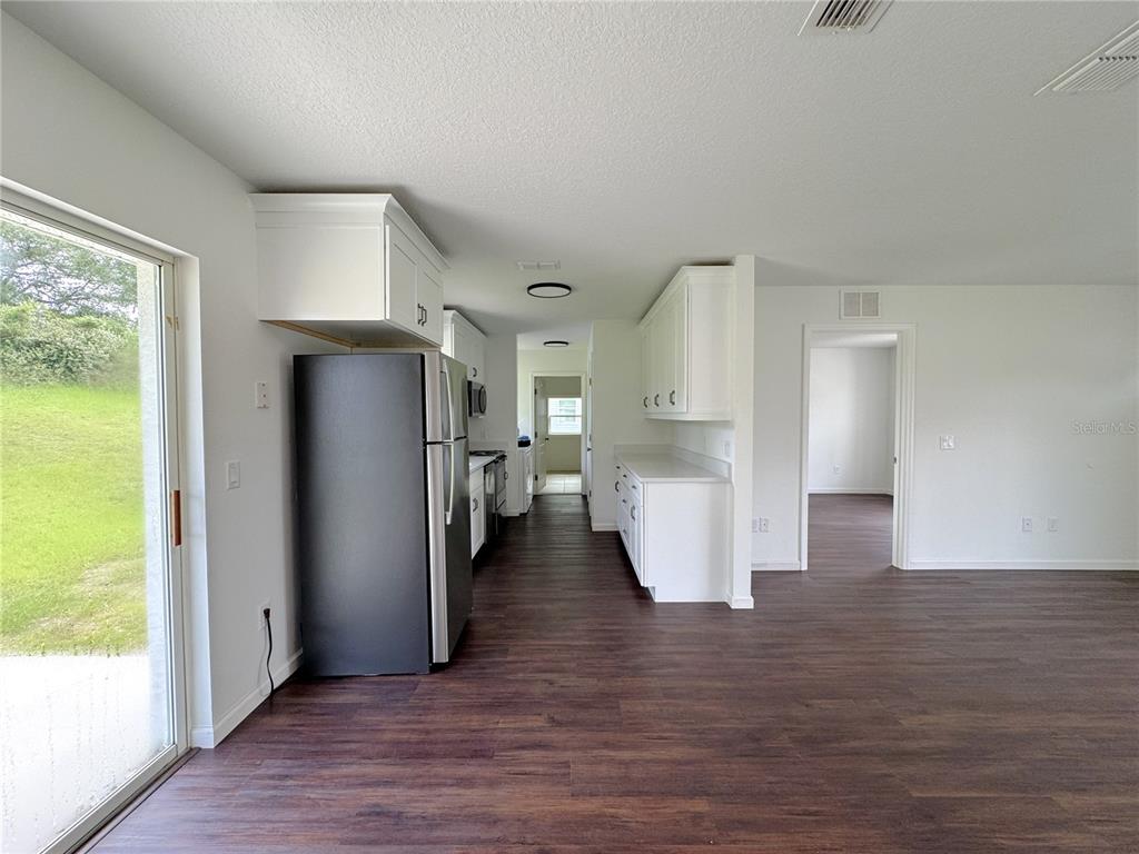 A kitchen with white cabinets and a black refrigerator opens to a living area — 102 EDISON STREET, INVERNESS, FL