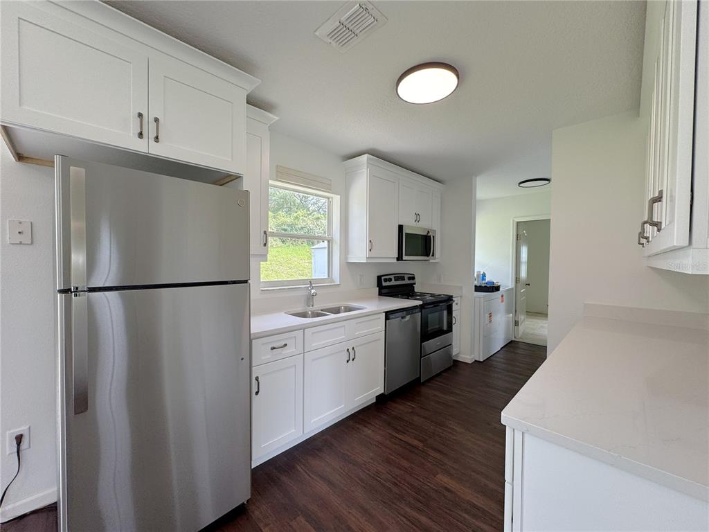 A kitchen features white cabinetry, stainless steel appliances, a window, and dark wood-look flooring — 102 EDISON STREET, INVERNESS, FL