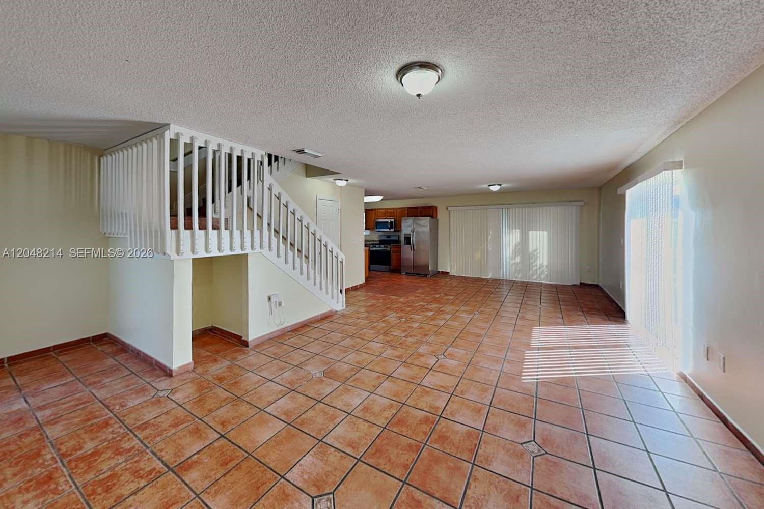 An open-concept living area features a staircase, tile flooring, and a kitchen in the background — CUTLER BAY, FL