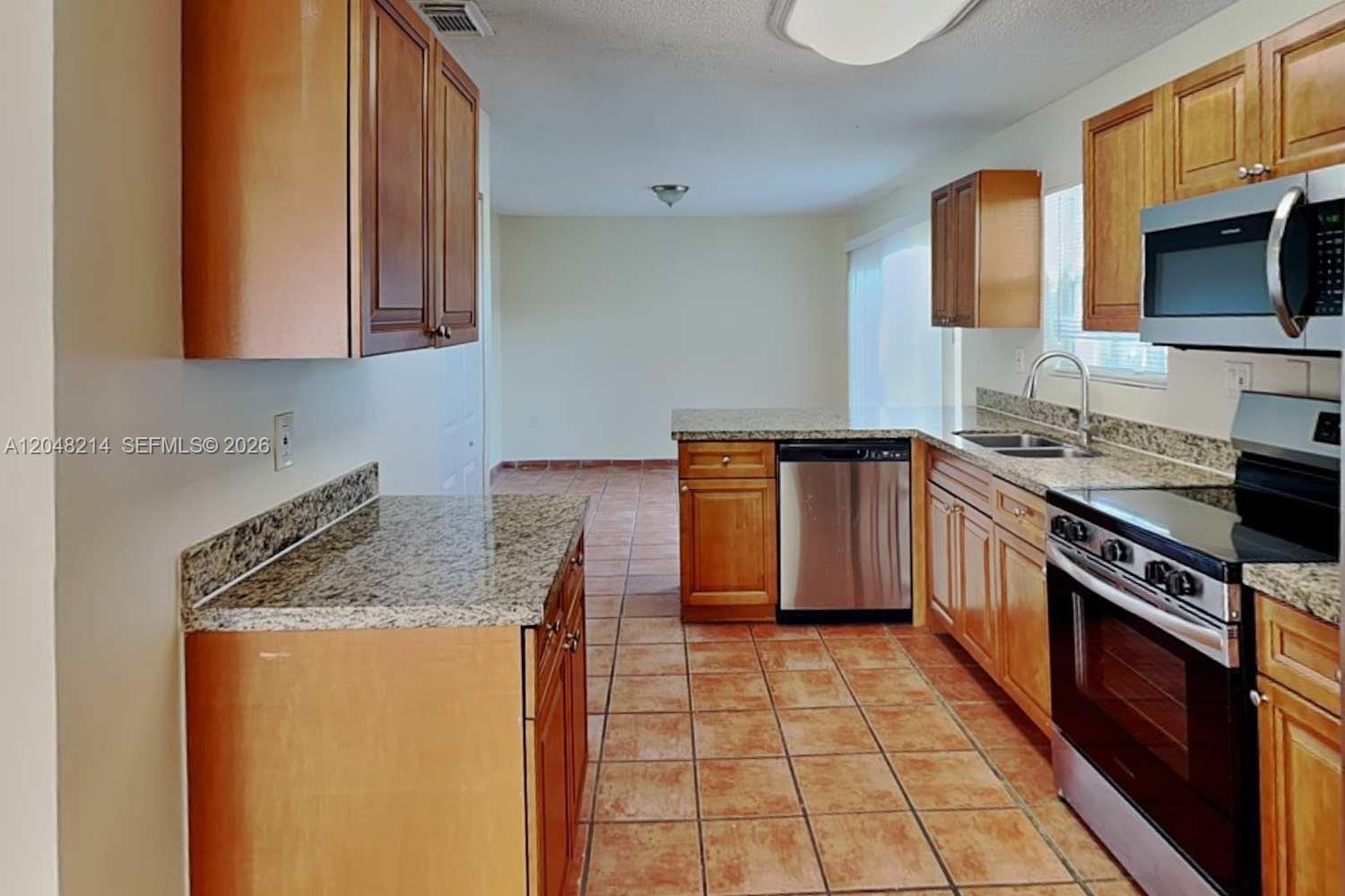 A kitchen features wood cabinets, granite countertops, stainless steel appliances, and tile flooring — CUTLER BAY, FL