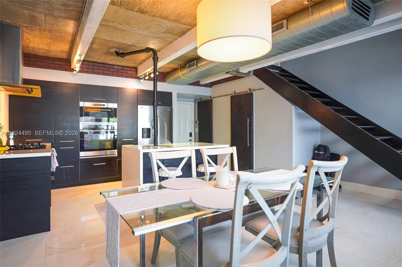 A modern kitchen and dining area feature dark cabinetry, a glass table, and exposed ductwork — 18101 NW 68th Ave # C204, Hialeah FL 33015, HIALEAH, FL