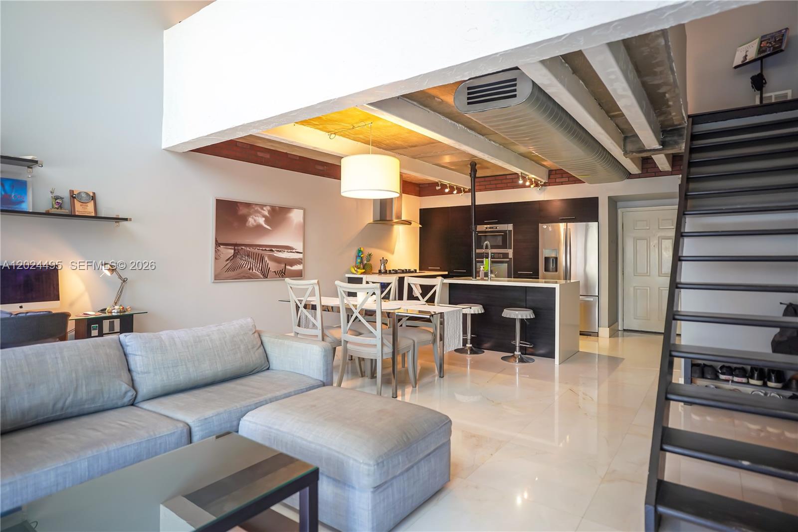 An open-concept living and dining area features a modern kitchen, industrial ceiling, and staircase — 18101 NW 68th Ave # C204, Hialeah FL 33015, HIALEAH, FL