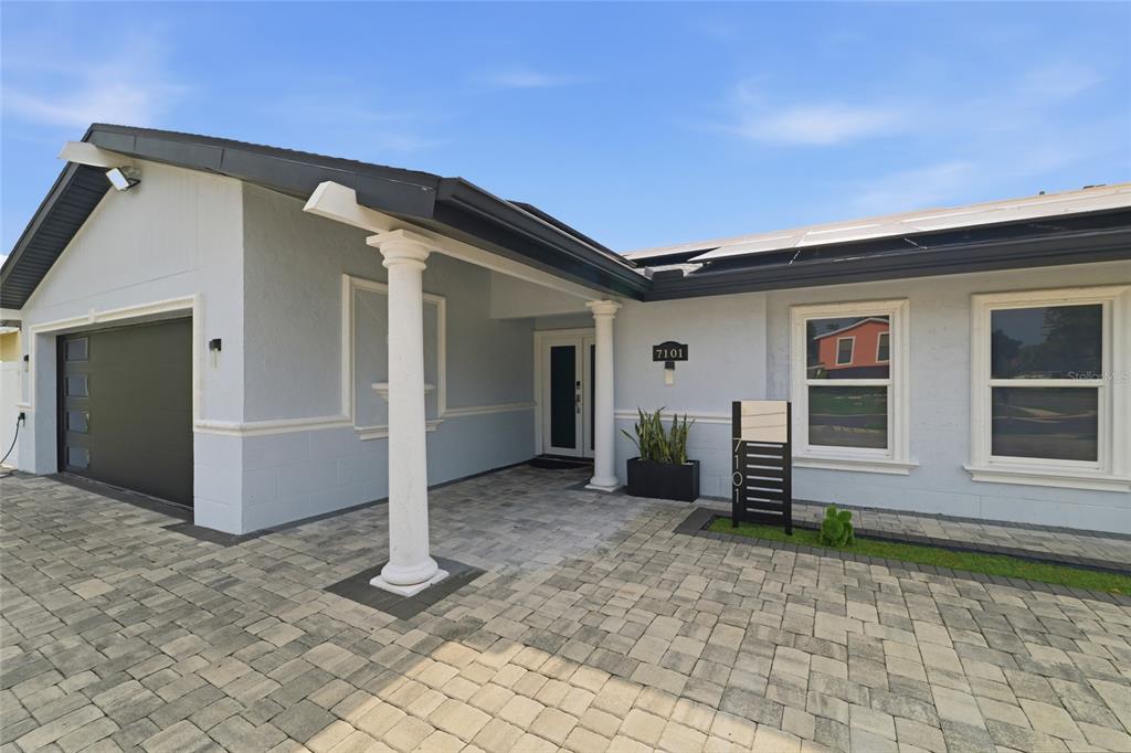 A light blue house exterior features a paved driveway, a covered entryway, and solar panels — 7101 SHENANDOAH COURT, TAMPA, FL