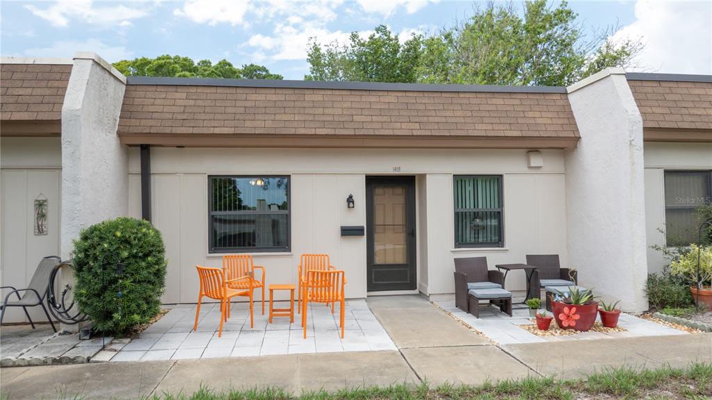 The exterior of a single-story townhouse features a paved patio, orange chairs, and a front door — 1418 ARROWHEAD CIRCLE W UNIT 20D, CLEARWATER, FL