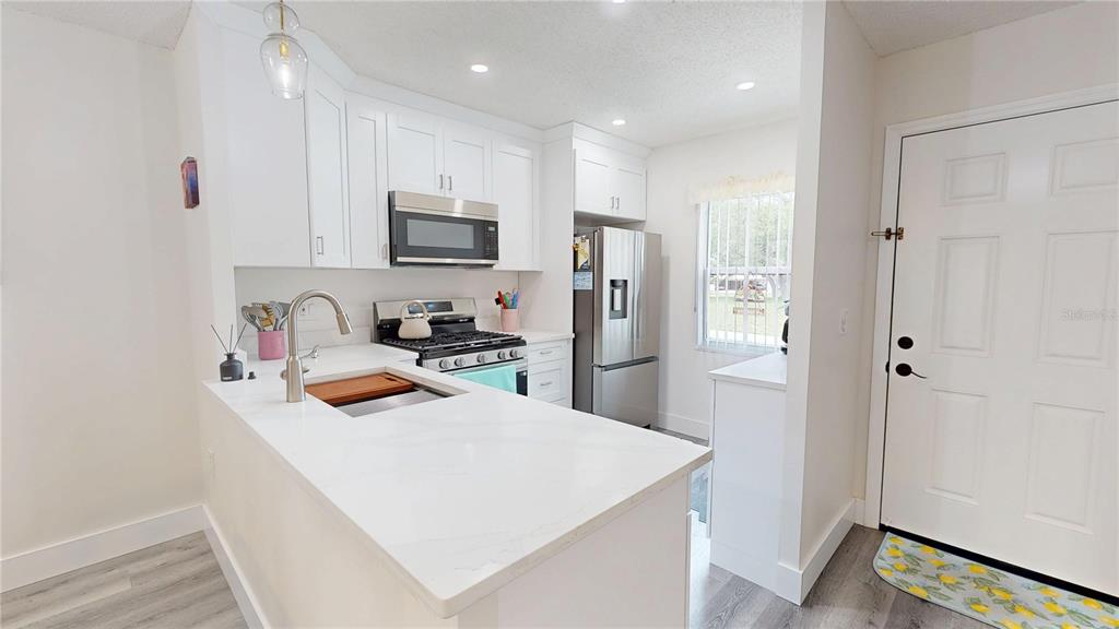 A kitchen features white cabinets, stainless steel appliances, a quartz countertop, and a white door — 1418 ARROWHEAD CIRCLE W UNIT 20D, CLEARWATER, FL