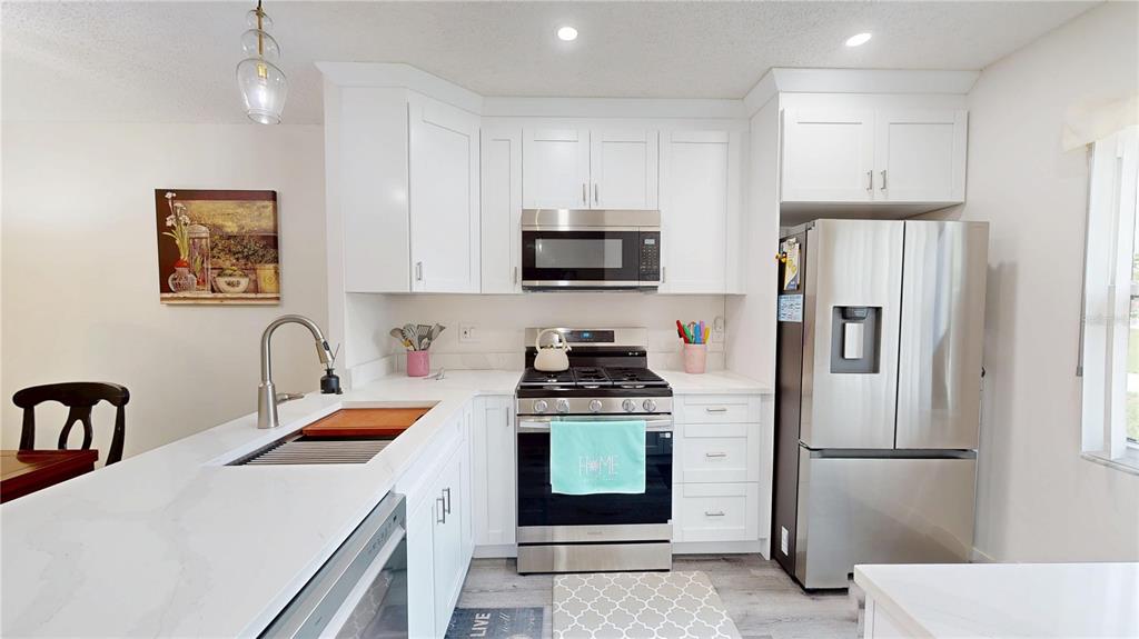 A modern kitchen features white cabinets, stainless steel appliances, and a white quartz countertop — 1418 ARROWHEAD CIRCLE W UNIT 20D, CLEARWATER, FL